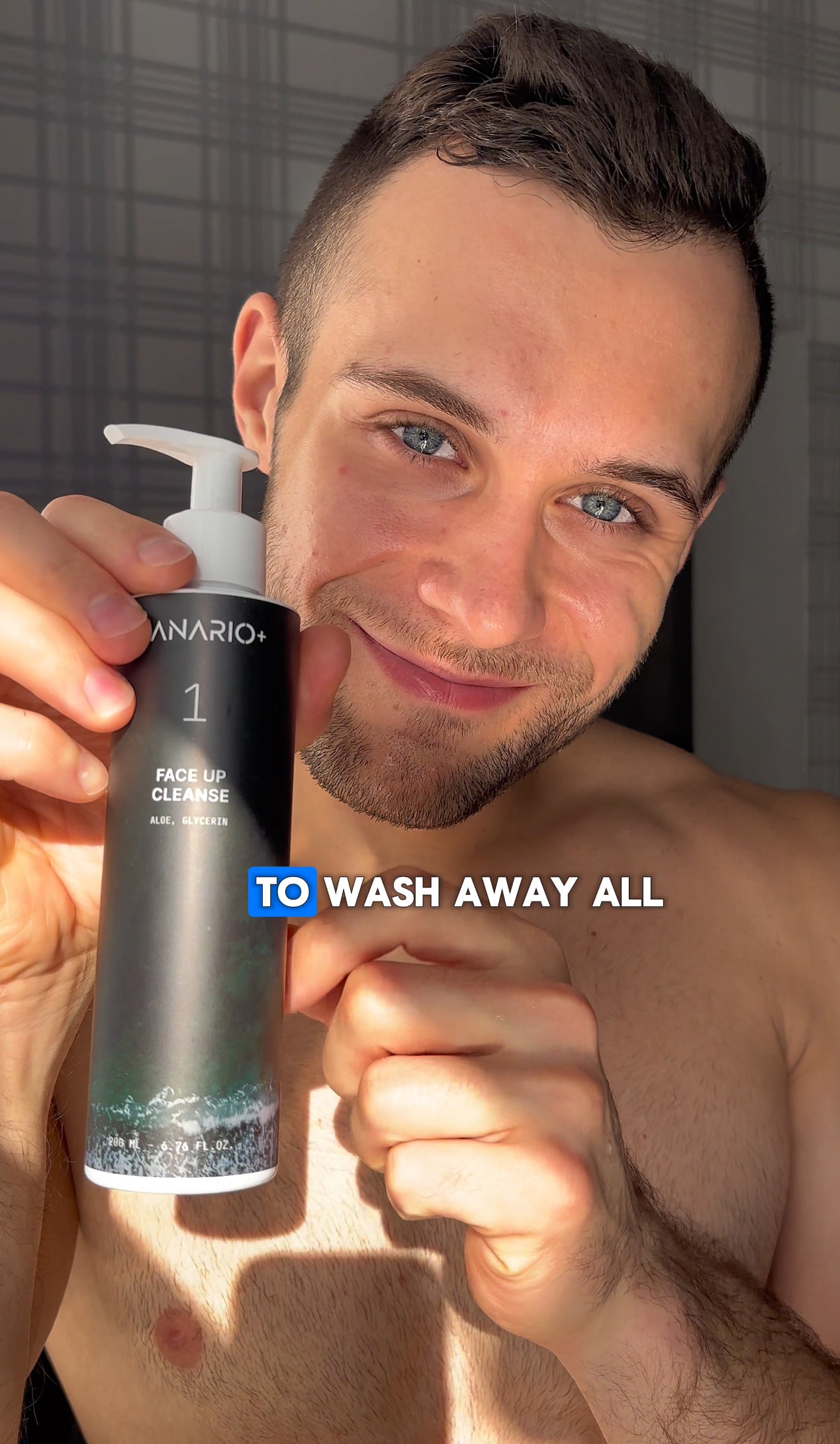 Image of Fitness Body Builder holding a 200ml Face Up Cleanse, post work out, to wick away oil, dirt and grime. Background is a bathroom with slanting light, to emphasize his translucent glow from within complexion and glass skin aesthetic. 